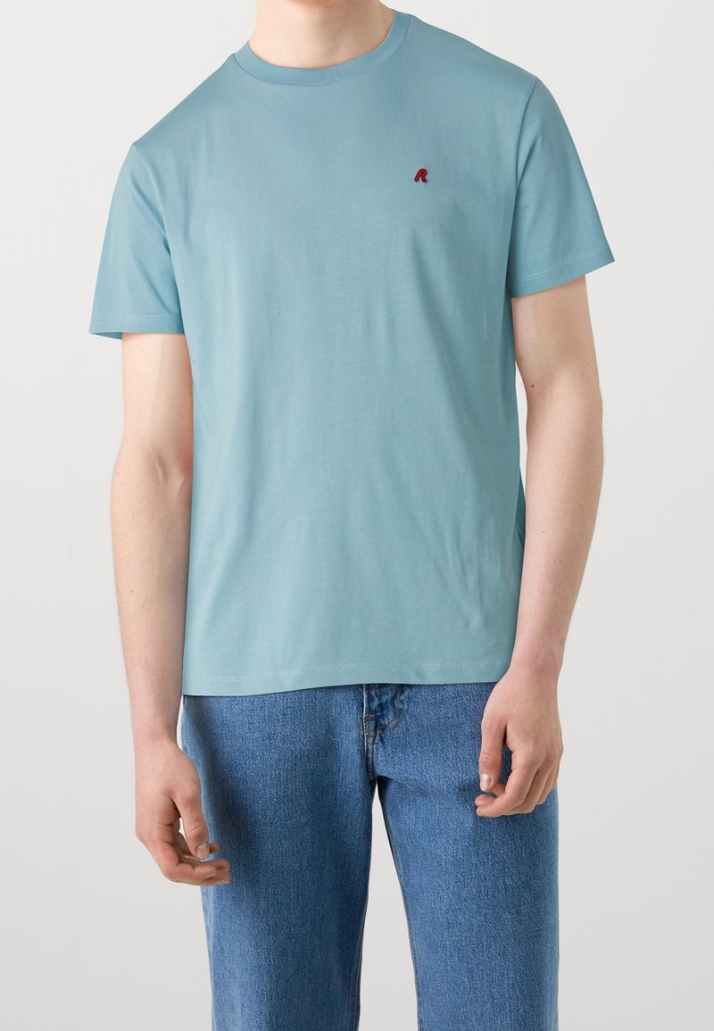T-shirt à manches courtes bleu clair en tissu doux, avec un petit logo rouge sur la poitrine gauche et un design classique à col rond.