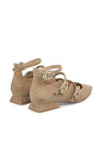 Chaussures beige en daim à talons bas avec des pointes effilées, ornées de plusieurs sangles décoratives et d'accents ressemblant à des bijoux sur les côtés.
