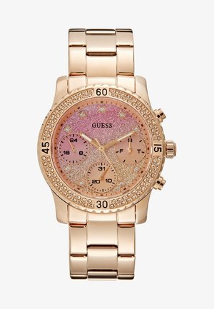 Montre-bracelet en métal or rose avec cadran rose pailleté, index en cristaux, trois sous-cadrans, et une lunette parée de cristaux, de la marque GUESS.