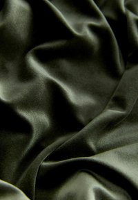 Material din catifea verde închis, cu pliuri moi și o textură netedă și lucioasă, care captează lumina din unghiuri diferite.