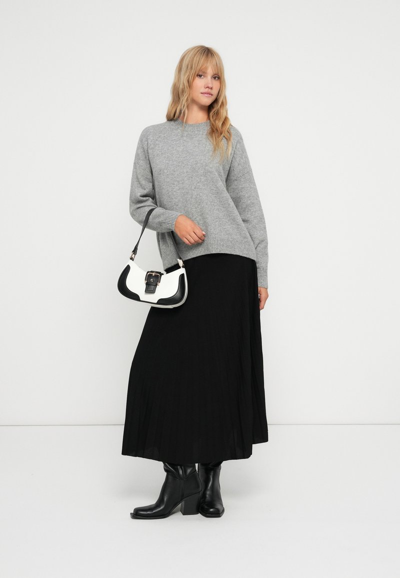 Szary dzianinowy sweter, czarna plisowana spódnica, czarne botki na obcasie oraz biała torebka z czarnymi akcentami; minimalistyczny design i miękkie tekstury.