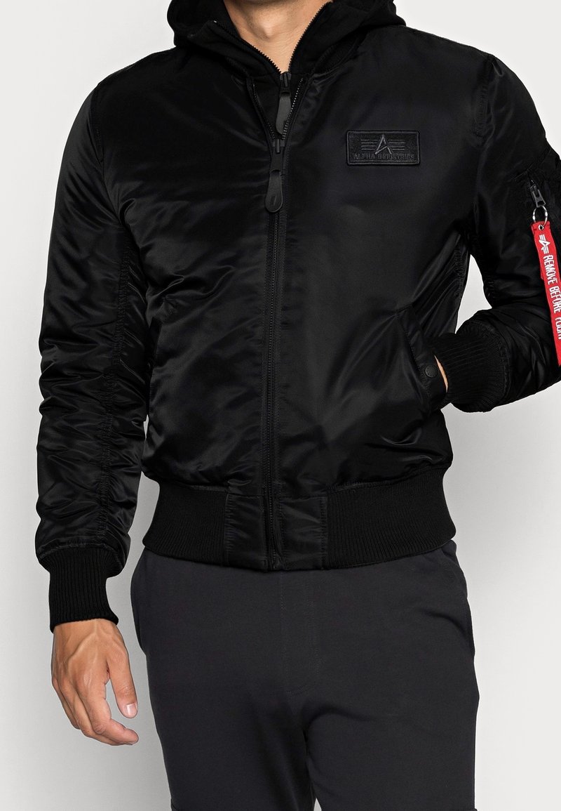 Giubbotto bomber nero con zip frontale, cappuccio, polsini e orlo a costine, tasca laterale e una fascia rossa a contrasto. Materiale liscio e lucido.