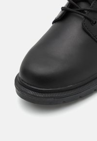 Svart lädersko med rund tå, strukturerad sula och runda snören. Har en slät överdel och en ribbad sula för bra grepp.