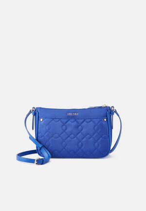 Blauwe doorgestikte crossbodytas met verstelbare riem, ritssluiting en klein metalen logo 'Anna Field' aan de voorkant.