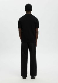 Svart kortärmad polo shirt i texturerat material, ihop med löst sittande svarta byxor. Enkel, minimalistic design.