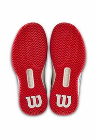 Suelas de goma roja con un patrón de relieve ondulado y el logo blanco de Wilson. Bordes redondeados, paredes laterales beige y diseño de tacón plano.