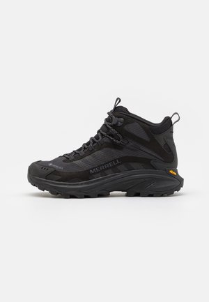 Bota de caminhada Merrell em preto. Apresenta parte superior sintética, colarinho acolchoado e sola Vibram. Painéis em rede para respirabilidade, design de amarração.