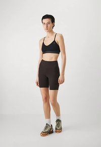 Juoda sportinė liemenėlė su plonomis petnešėlėmis, derinama su aukšto liemens rudos spalvos dviračių šortais, papildyta žaliais ir oranžiniais sportiniais bateliais.