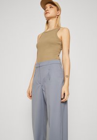 Lichtbruine tanktop gecombineerd met hooggewaagde, losvallende lichtblauwe broeken. Zachte stof met minimale details.
