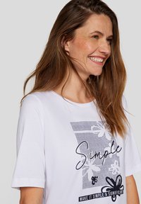Weißes Baumwoll-T-Shirt mit kurzen Ärmeln, das mit einem schwarzen grafischen Druck des Wortes "Simple" und floralen Designs versehen ist. Glatte Textur.