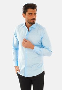 Camicia azzurro chiaro con maniche lunghe, dotata di polsini singoli e colletto standard. Texture liscia e silhouette aderente.