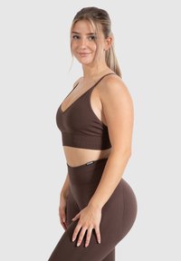 Braunes nahtloses Activewear-Set, bestehend aus einem Bralette mit verstellbaren Trägern und hochgeschnittenen Leggings, beide aus einem strukturierten, dehnbaren Material.