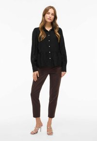 Crna, košulja na dugmad s napuhanima rukavima i slojevitim rubom. Uparena s smešnim, uskim hlačama i srebrnim sandalama na petu. Glatka tkanina.