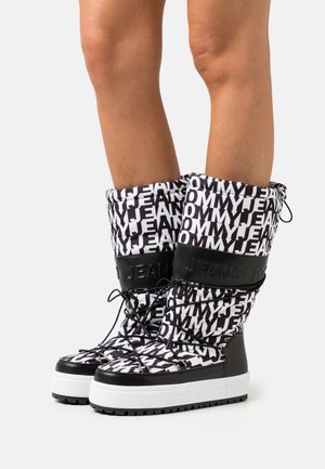 Černobílé vysoké kozačky přes kolena s polstrovaným svrškem s opakujícím se vzorem textu a černými gumovými doplňky. Podrážka na platformě a detaily se šněrováním.