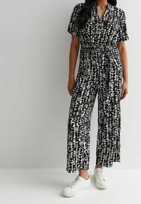 Mono impreso en blanco y negro con mangas cortas, cinturilla ajustable y diseño de pierna ancha. Combinado con zapatillas blancas para un look informal.