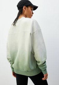 Hanorac supradimensionat cu un gradient de gri deschis și verde, cu manșete și tiv nervurate, având un design clasic cu guler rotund și o textură moale.