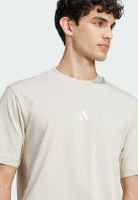 Μπεζ βαμβακερό t-shirt με κοντά μανίκια, με λευκό κεντητό λογότυπο στο αριστερό στήθος. Λείος υφασμάτινος σχεδιασμός, κλασικός λαιμός τύπου crew neck.