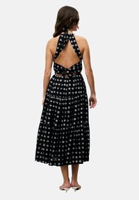 Schwarzes Halterkleid mit floralem weißen Druck, offenes Rückendesign, gebundenem Hals- und Taillenband, mit einem gestuften Rock und fließender Textur.