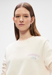 Κρέμα φούτερ με στρογγυλή λαιμόκοψη, ριμπ μανσέτες και μπροστινό γραφικό σε παστέλ αποχρώσεις που γράφει "TOMMY JEANS Νέα Υόρκη".