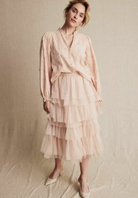 Ljusrosa, lager-på-lager-tärning kjol med volanger, kombinerad med en matchande blus som har texturerad blommig broderi och en v-ringning.