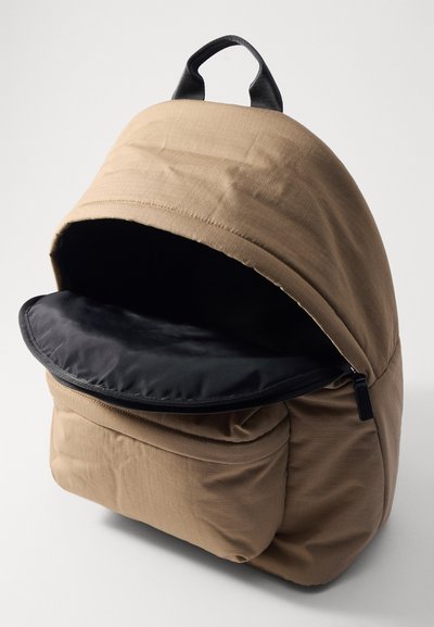 Brauner Rucksack mit abgerundeter Oberform, einem schwarzen Reißverschluss und einem strukturierten Außenmaterial. Enthält eine Vordertasche und einen oberen Griff.