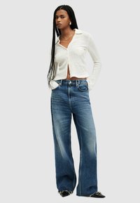 Camicia bianca a maniche lunghe con colletto, abbinata a jeans a gamba larga blu chiaro. Accentuata con una cintura e scarpe nere a punta.