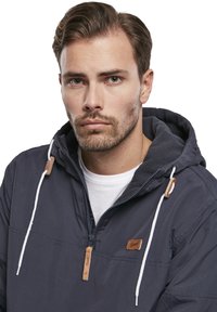Chaqueta pullover azul oscuro con cordones blancos, acentos de cuero y un diseño de media cremallera. Presenta un forro interior cálido y texturizado.