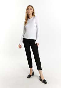 Witte blouse met lange mouwen en een aansluitend ontwerp, gecombineerd met zwarte tapered trousers. Zwarte schoenen met een lage hak en decoratieve accenten.