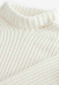 Weißer Strickpullover mit einem gerippten Rollkragen und strukturierten vertikalen und diagonal gestrickten Mustern.