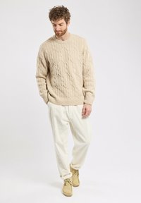 Maglione beige lavorato a maglia con motivi a treccia, vestibilità ampia, collo rotondo, abbinato a pantaloni crema e stivaletti in suede beige. Texture liscia in tutto il capo.