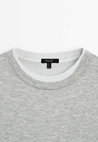 Pull gris à col rond avec col intérieur blanc et étiquette de taille indiquant petite taille en EUR, USA et MEX.