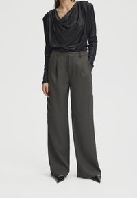 Maglietta nera a maniche lunghe con scollatura drappeggiata, abbinata a pantaloni larghi grigi scuri a vita alta con tasche laterali e tessuto testurizzato.