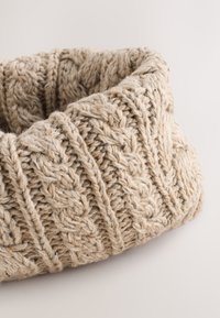 Bézs színű végtelenített kötött sál texturált kötélmintával és enyhe színfoltokkal. Puha, vastag fonalból készült, barátságos megjelenést kölcsönözve.