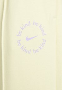 Světle žlutá mikina s kulatým potiskem s opakujícím se textem "buď laskavý" v levandulové barvě, vedle malého loga Nike v levandulové.