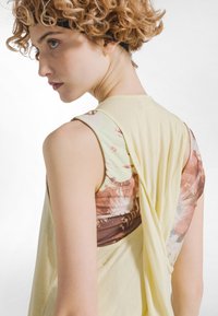 Lysegul ærmeløs top med en draperet ryg og en brun og flerfarvet mønstret panel. Glat tekstur, afslappet pasform.