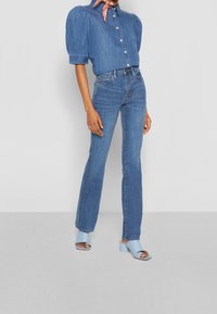 Camisa de mezclilla con mangas abullonadas, jeans de color azul claro y mules con tacón de color azul claro. Camisa abotonada, jeans ajustados a la cintura, estilo casual.