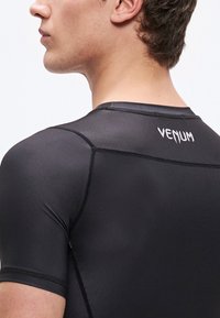 Μαύρο αθλητικό μπλουζάκι με κοντά μανίκια και το λογότυπο της Venum στην πλάτη, με λείο υλικό, εφαρμοστή σχεδίαση και αντίθετες ραφές.