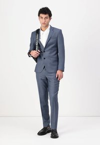 Blauer karierter Anzug mit passender Hose, taillierte Passform, Ein-Knopf-Blazer und weißem Hemd; Model hält eine schwarze Markenhandtasche.