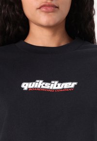 T-shirt nera in cotone con logo bianco e rosso "quiksilver BOARDRIDING COMPANY" sul petto, con scollatura rotonda classica.
