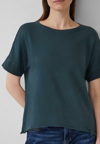 Donkergroen t-shirt met korte mouwen en een brede halslijn, van textuurstof met een subtiele logo op de zoom. Ontspannen pasvorm met opgerolde mouwen.