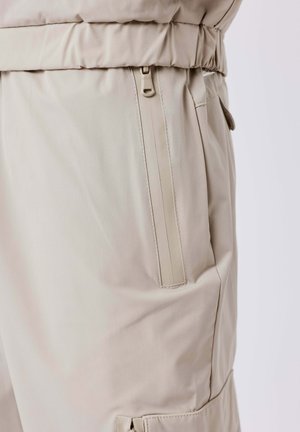 Pantaloni beige chiaro con tasca laterale con zip, vita elastica e tessuto liscio.