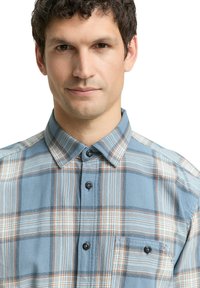 Lichtblauwe geruite shirt met een knoopsluiting, lange mouwen en een borstzak. Gegolfde stof met bruine en witte accenten.