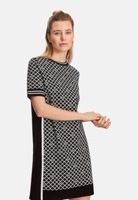 Schwarz-weißer Strickkleid mit geometrischem Muster, kurzen Ärmeln und geripptem Kragen, mit kontrastierenden Seitenpanelen.