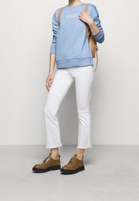 Sudadera de cuello redondo azul claro con el logo bordado "HUGO", combinada con jeans blancos recortados y zapatos de cuero marrón con suelas negras.