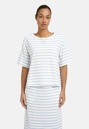 Woman wearing a white short-sleeve top and matching skirt with light blue horizontal stripes, standing against a plain background.