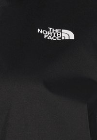 Maglietta nera a maniche corte realizzata in un tessuto testurizzato, con un logo bianco "The North Face" sulla parte sinistra del petto.