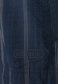 Granatowy materiał z pionowymi zielonymi i białymi paskami, z haftowanym logo "adidas" w zaokrąglonym prostokącie na dole.