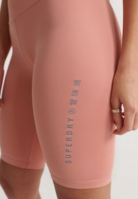Rosa, åtsittande cykelshorts i elastisk tyg, med en sidologo i grått och en slät, matt yta med kontrasterande sömdetaljer.