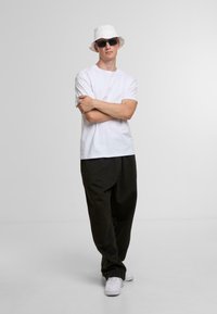White crew neck t-shirt, black loose-fit pants, white sneakers, and a white bucket hat with dark sunglasses. Plain design, casual style.
