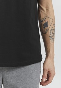 Camiseta de algodón negra con mangas cortas, con una textura suave. Se ven pantalones de chándal grises, hechos de una tela suave y mezclada.
